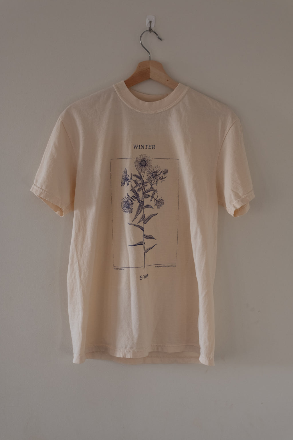 Beige t-shirt with floral design on a hanger against a plain wall