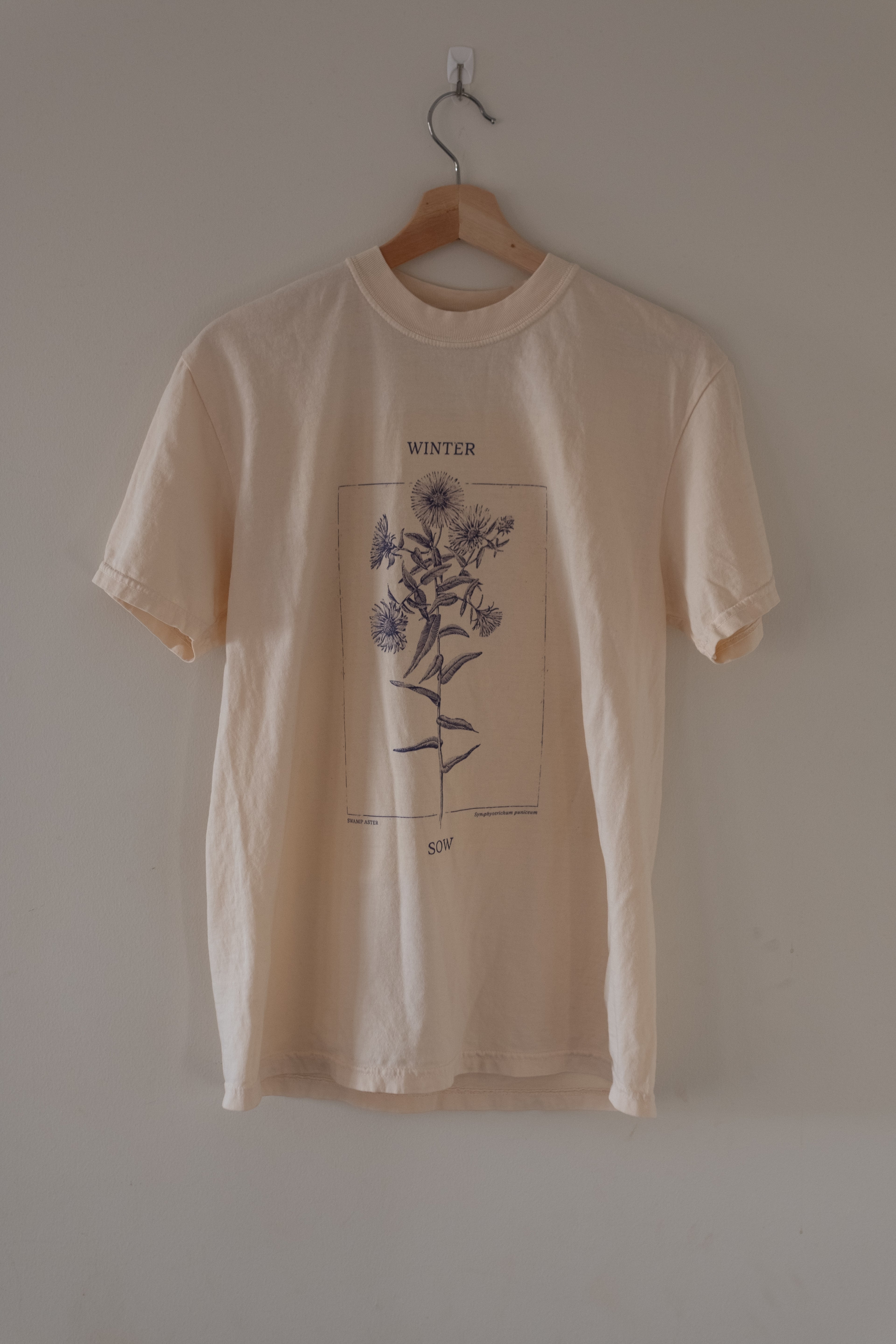 Beige t-shirt with floral design on a hanger against a plain wall